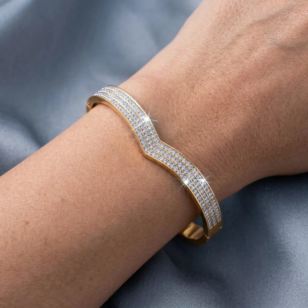 Gold bracelet with clear stones on a wrist against a gray background