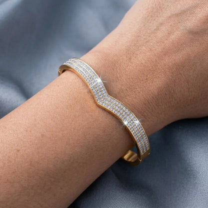Gold bracelet with clear stones on a wrist against a gray background