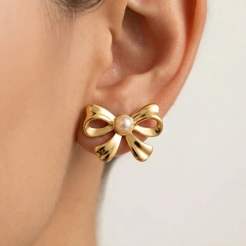 Gold bow-shaped earring with a pearl center worn by a person.