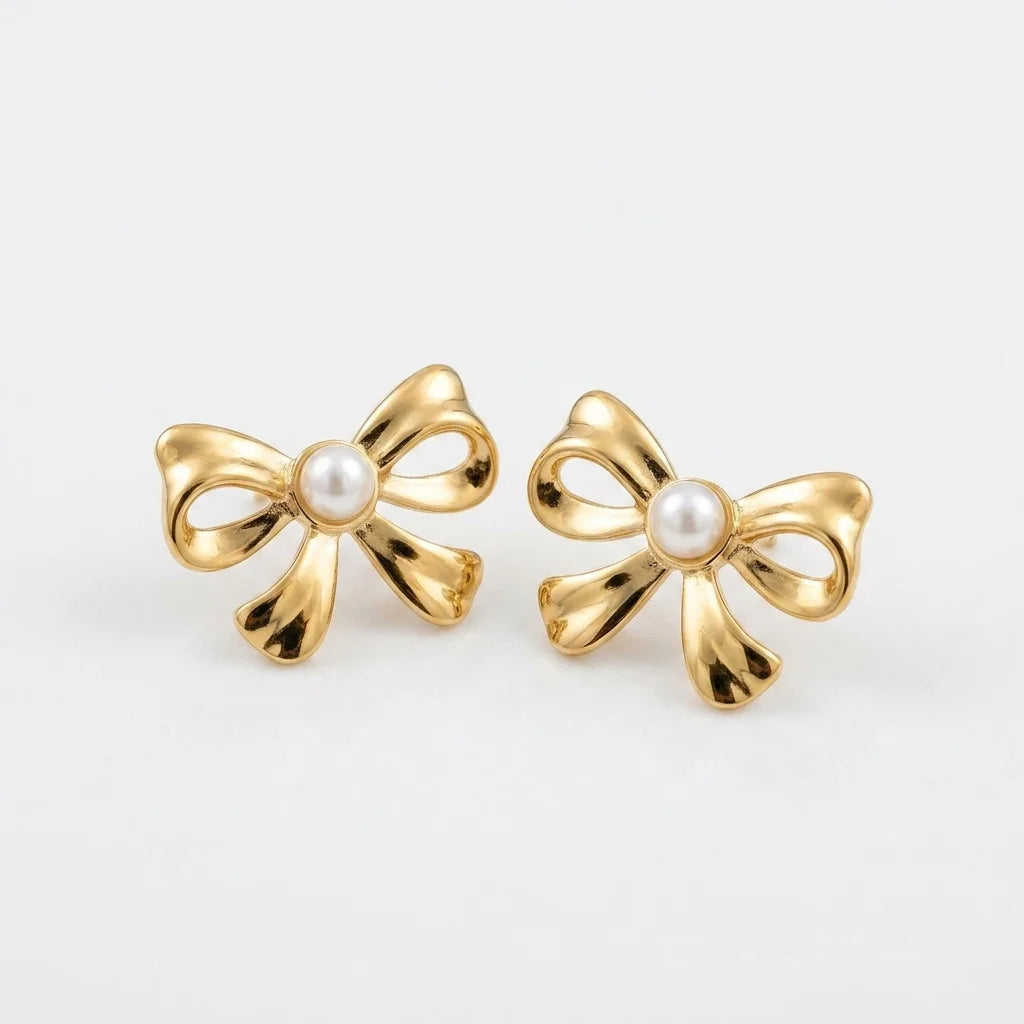 Gold bow-shaped earrings with pearl centers on a light gray background