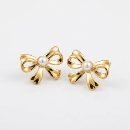 Gold bow-shaped earrings with pearl centers on a light gray background