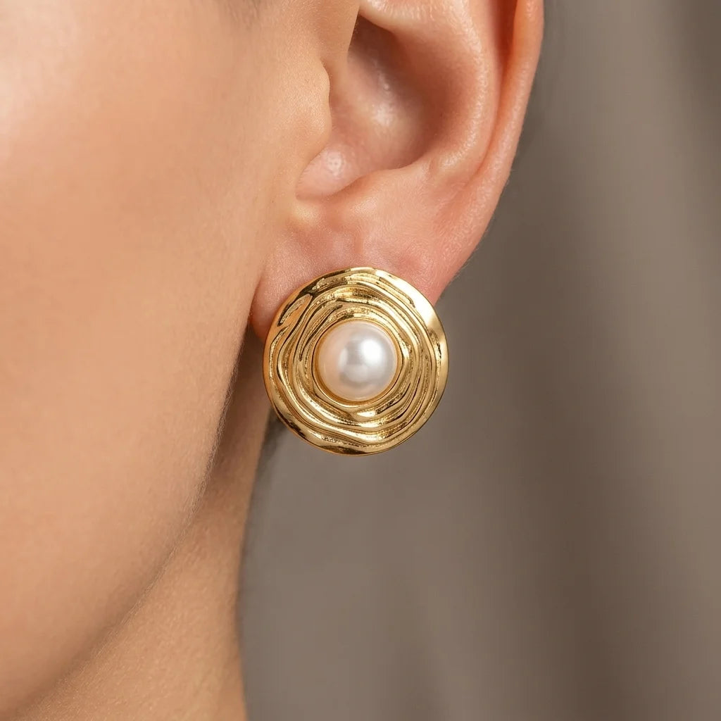 Gold earring with a pearl on an ear against a neutral background