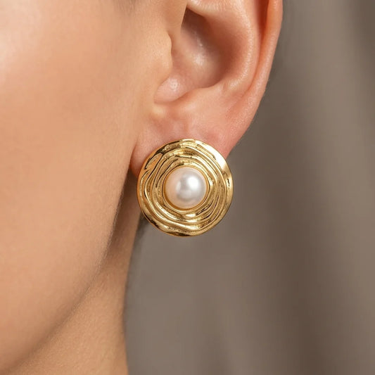 Gold earring with a pearl on an ear against a neutral background