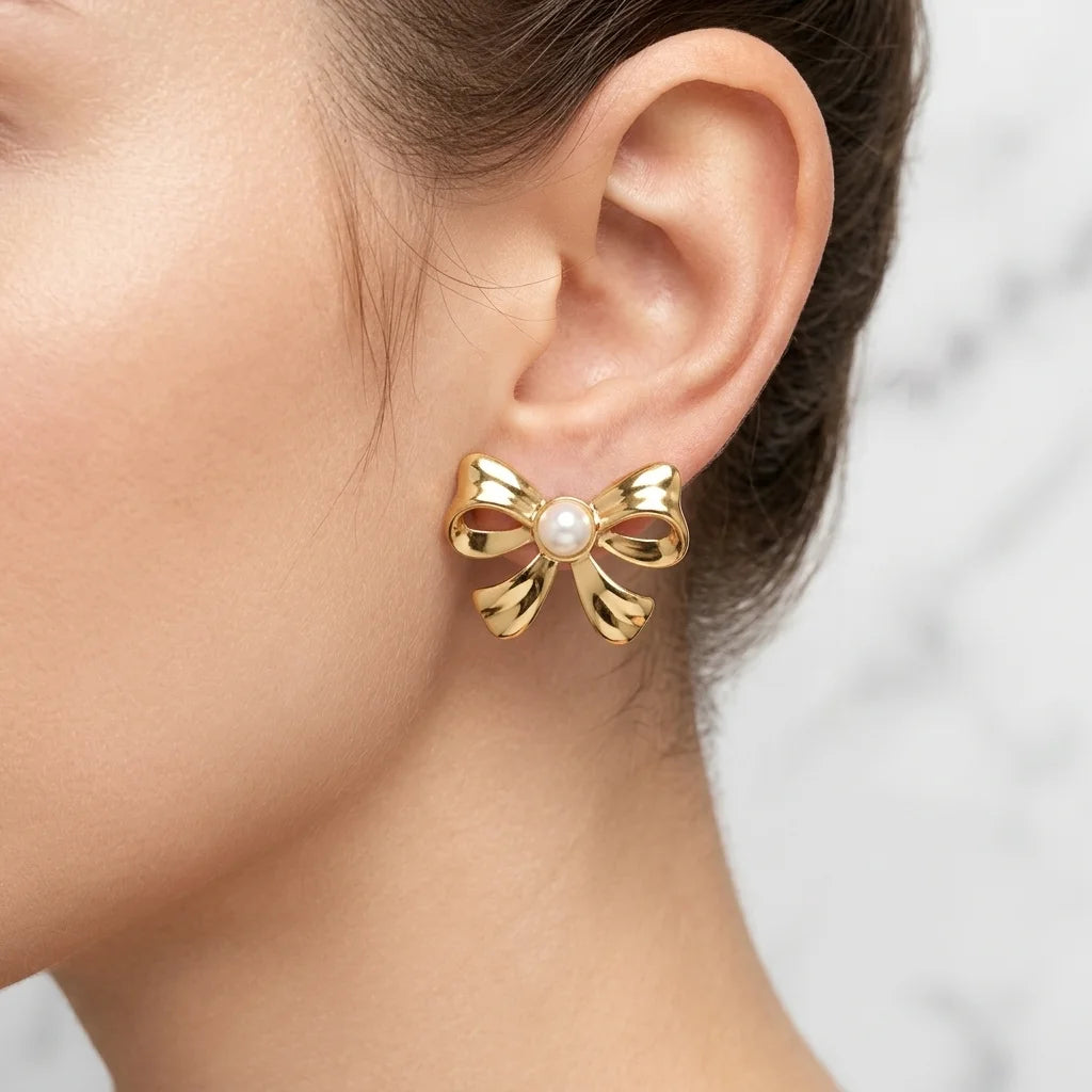 Gold bow-shaped earring with a pearl center worn by a person.