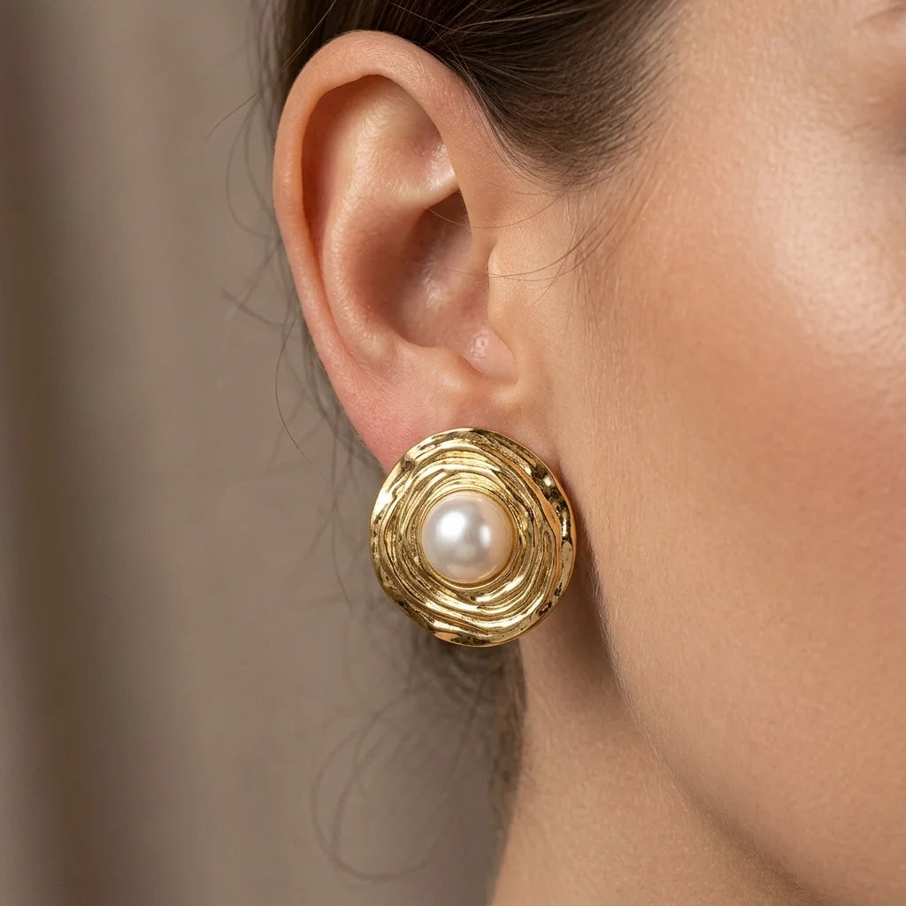 Gold earring with a pearl on an ear against a neutral background