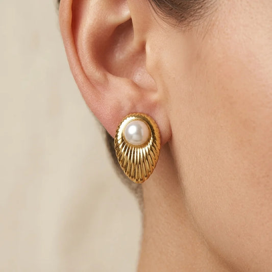 Gold earring with a pearl on an ear against a neutral background