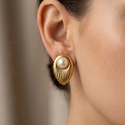 Gold earring with a pearl center worn by a person against a neutral background