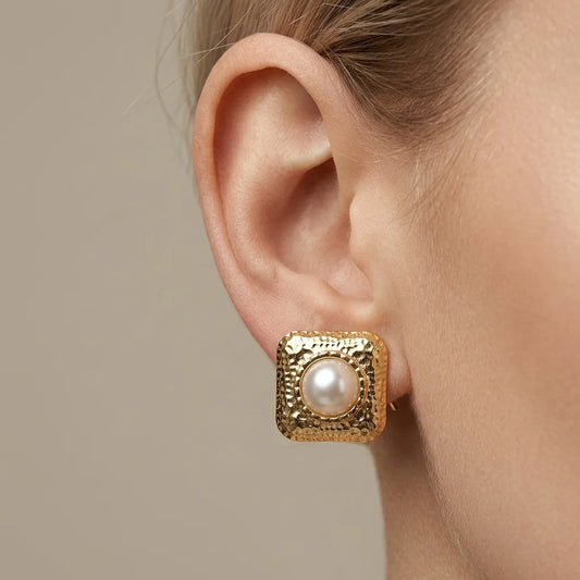 Gold earring with a pearl on an ear against a neutral background