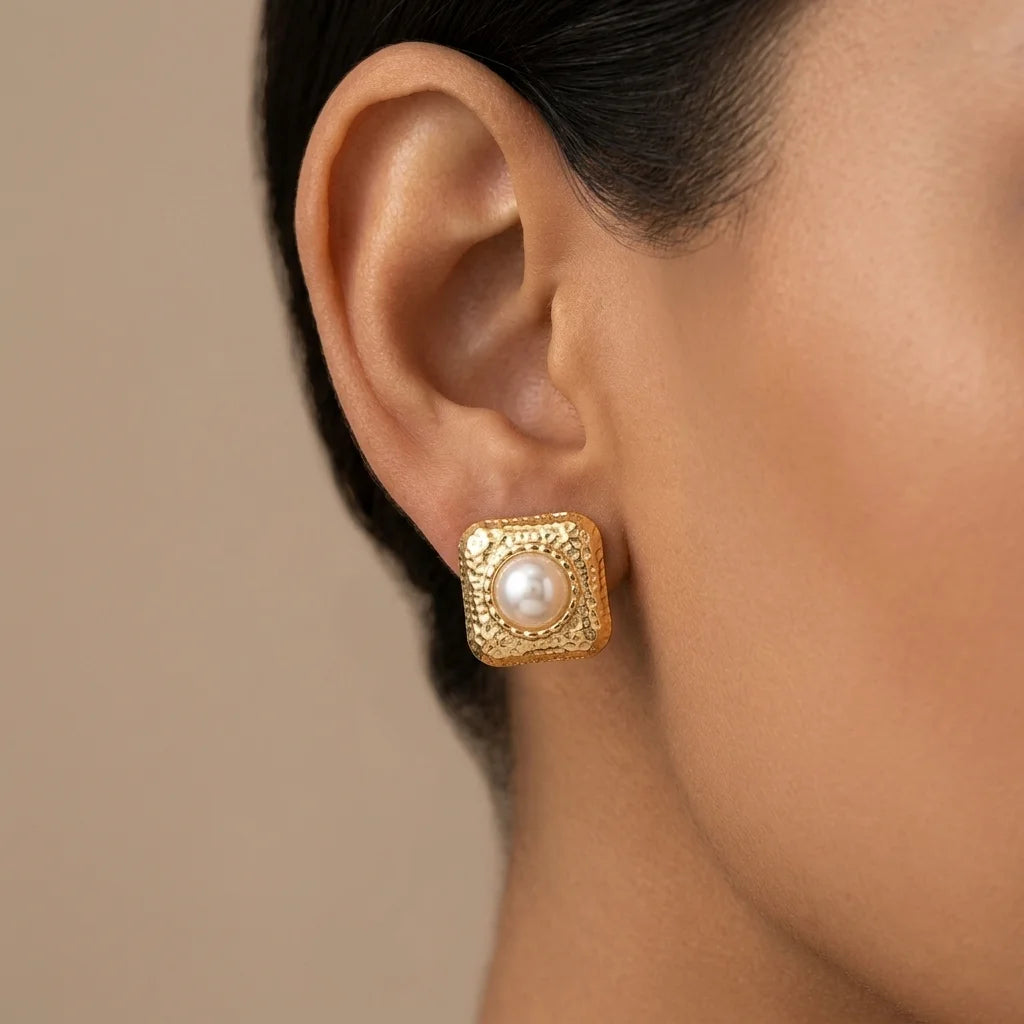 Gold earring with a pearl on an ear against a neutral background