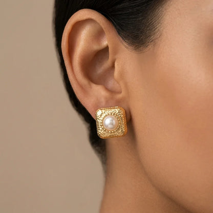 Gold earring with a pearl on an ear against a neutral background