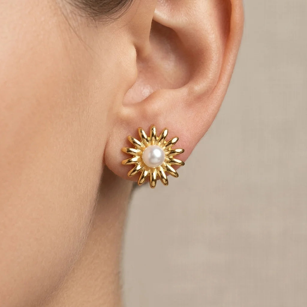 Gold sunflower-shaped earring with a pearl center worn by a person.