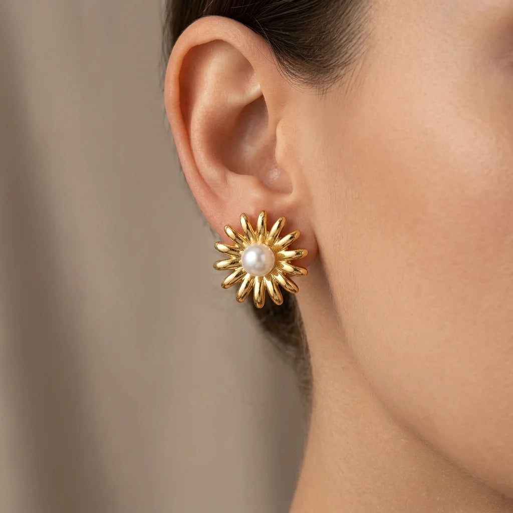Gold sunflower-shaped earring with a pearl center worn by a person.