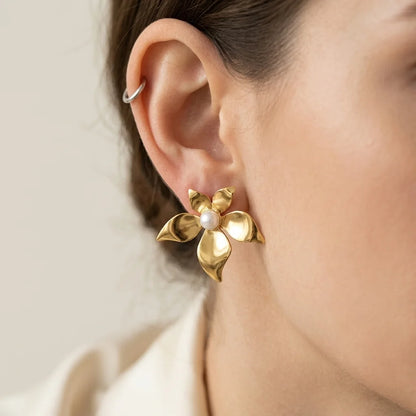 Gold flower-shaped earring with pearl center worn by a person.