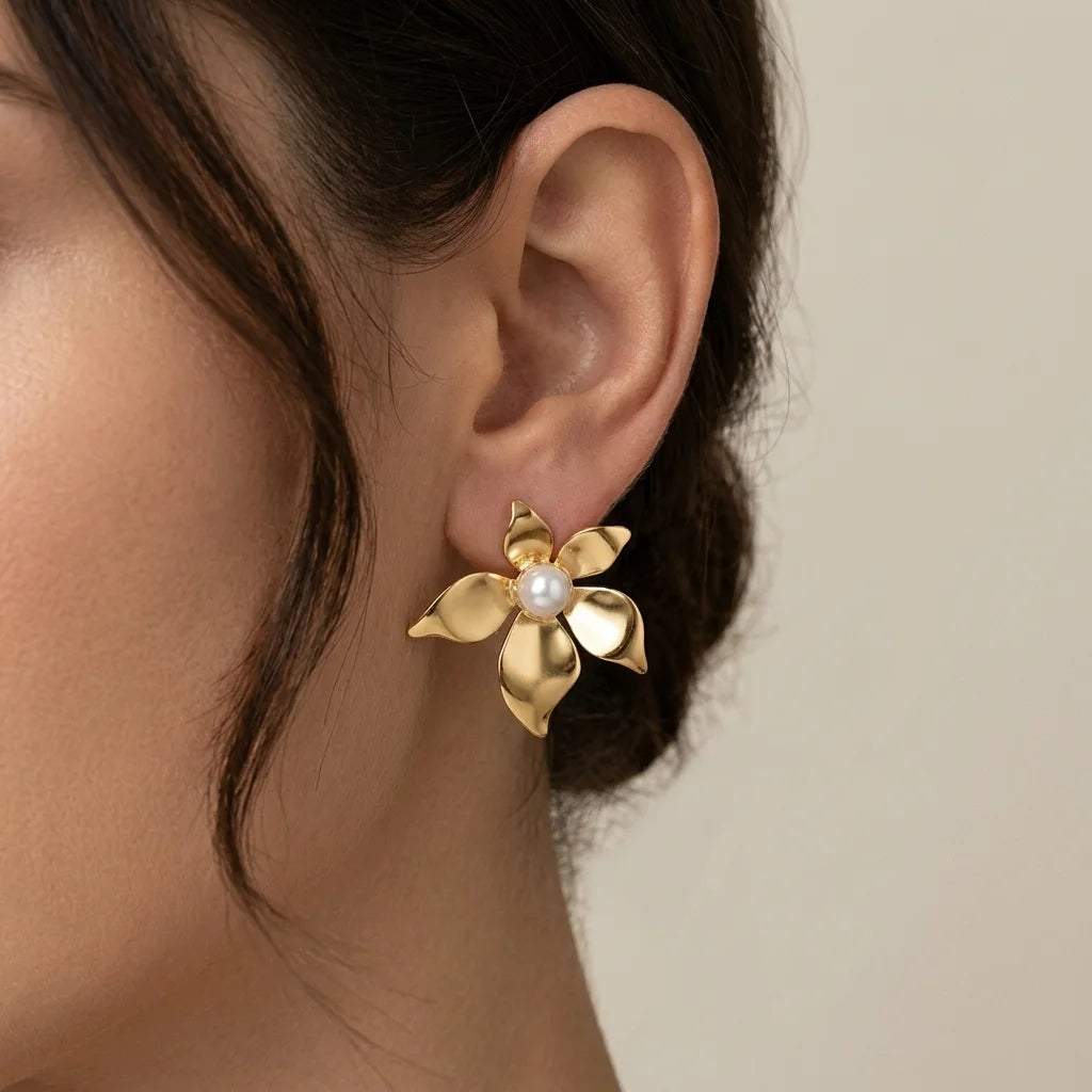 Gold flower-shaped earring with a pearl center worn by a person against a neutral background