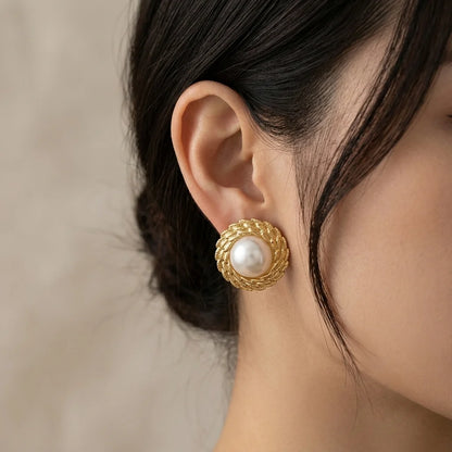 Gold earring with a pearl worn by a person against a neutral background