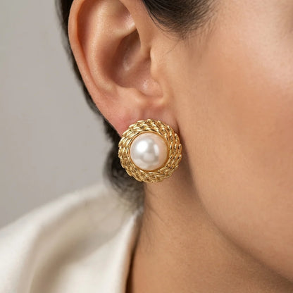 Gold earring with a pearl center worn by a person against a neutral background