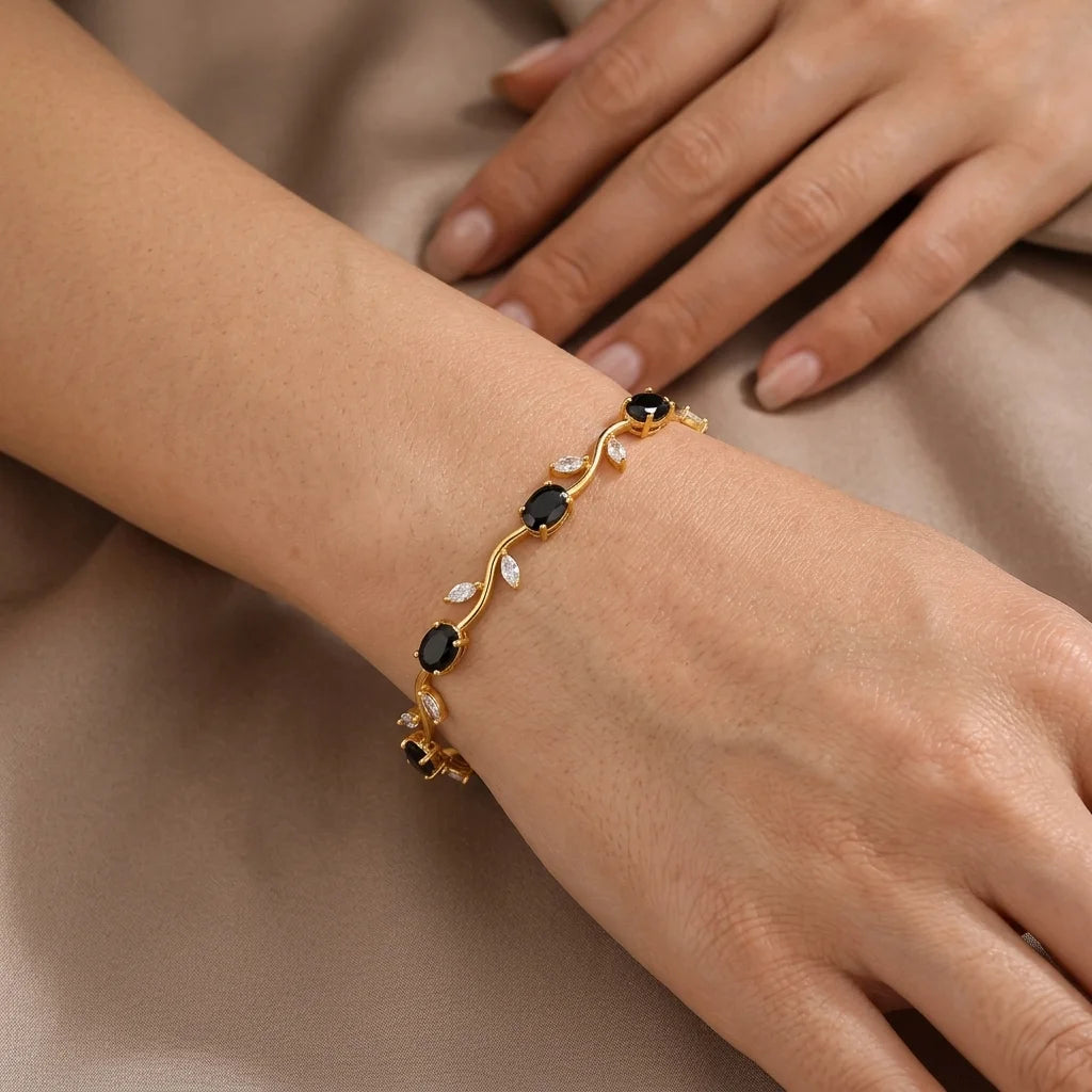 Gold bracelet with black stones on a wrist against a neutral background