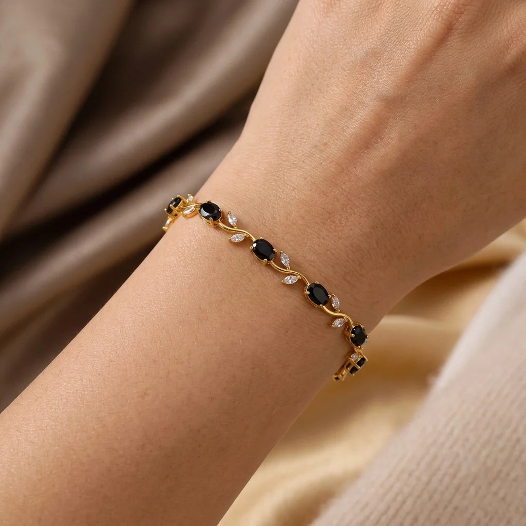 Gold bracelet with black stones on a wrist against a beige fabric background