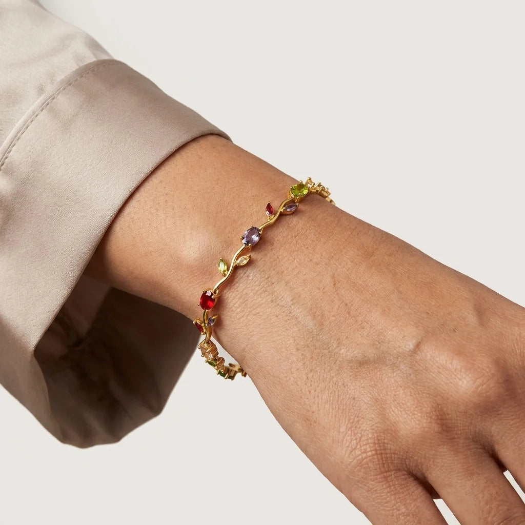 Gold bracelet with colorful beads on a wrist against a neutral background