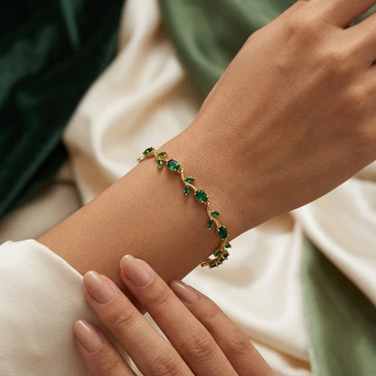Gold bracelet with green gemstones on a wrist against a neutral background