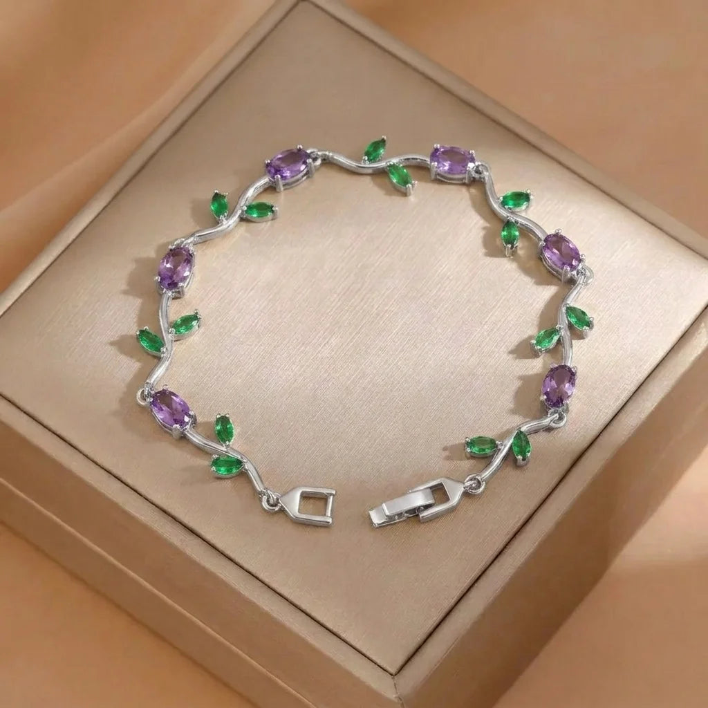 Silver bracelet with purple and green gemstones on a beige box