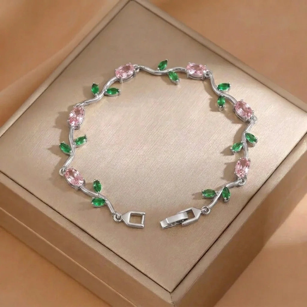 Silver bracelet with pink and green gemstones on a beige box
