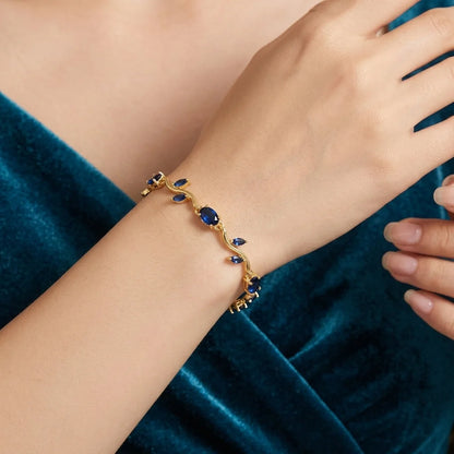 Gold bracelet with blue stones on a wrist against a blue velvet background