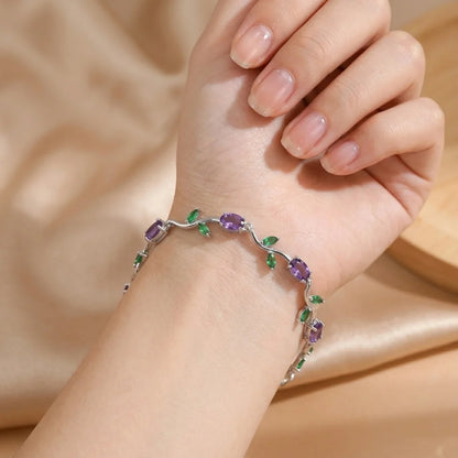 Hand wearing a bracelet with purple and green gemstones on a beige fabric background