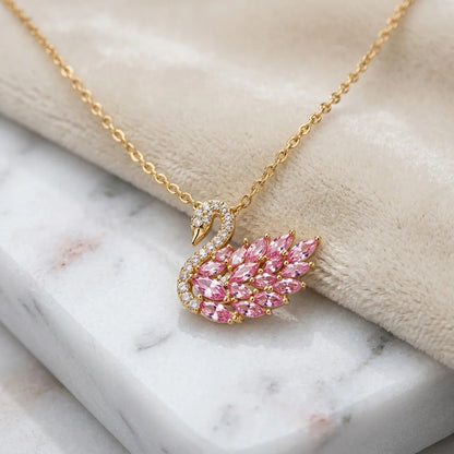 Gold necklace with a pink swan pendant on a marble surface
