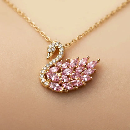 Gold necklace with a swan pendant featuring pink gemstones on a beige background