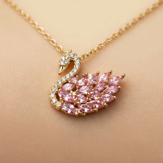 Gold necklace with a swan pendant featuring pink gemstones on a beige background