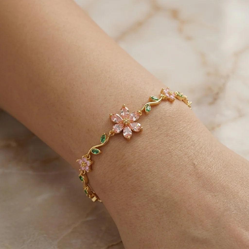Gold bracelet with pink floral charms on a wrist against a neutral background