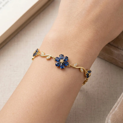 Gold bracelet with blue flower-shaped gemstones on a wrist against a neutral background