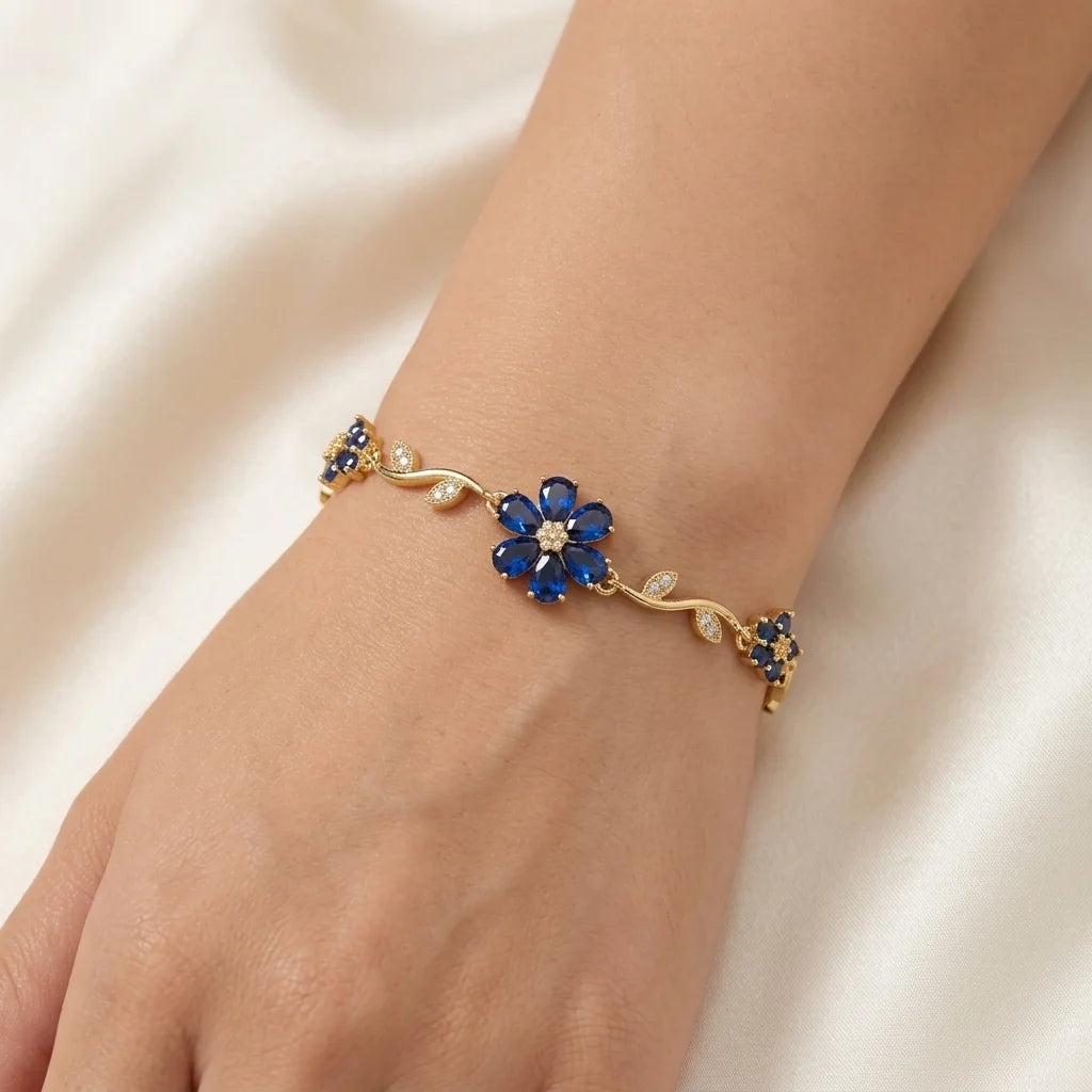 Gold bracelet with blue flower-shaped gemstones on a beige fabric background