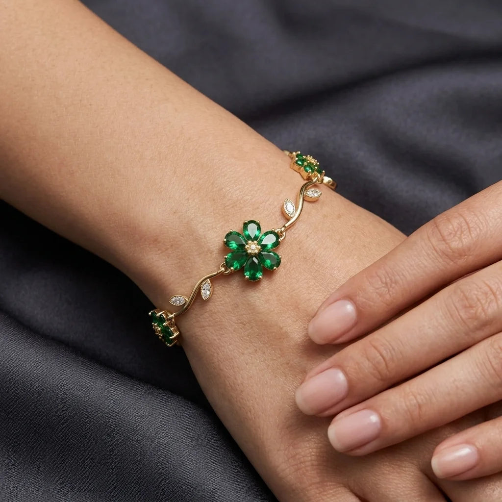 Gold bracelet with green gemstones on a wrist against a dark fabric background