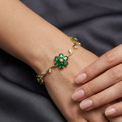 Gold bracelet with green gemstones on a wrist against a dark fabric background