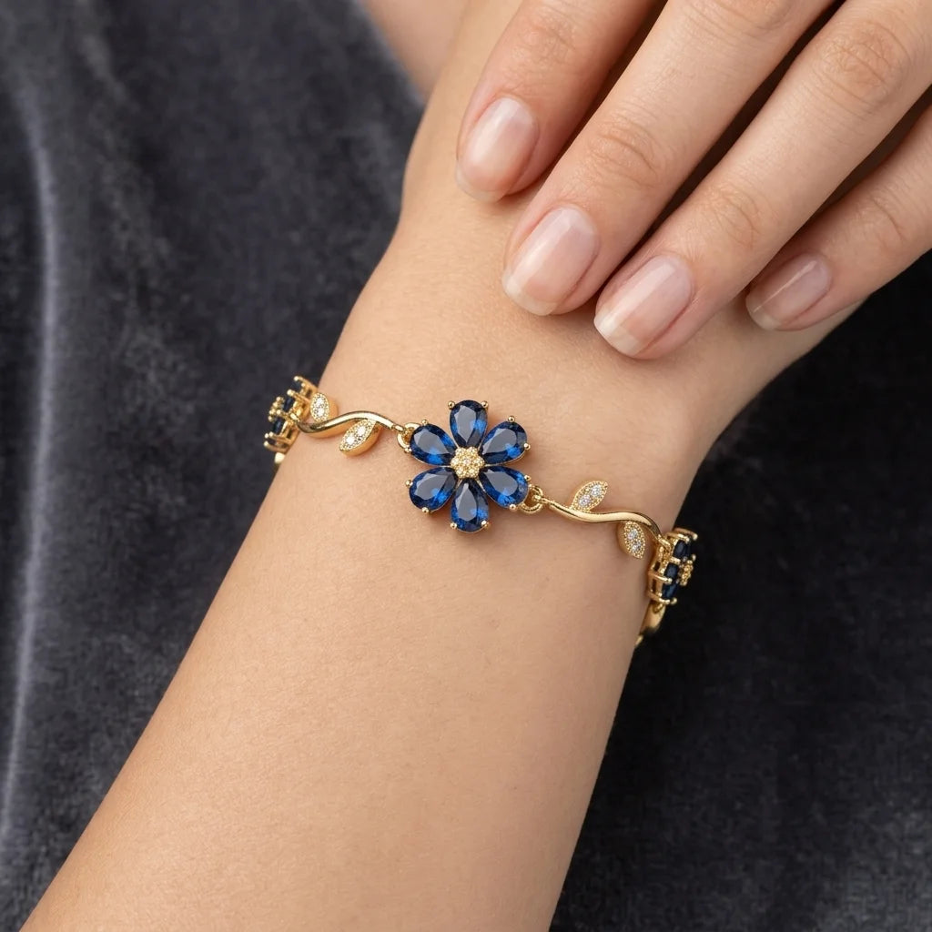 Gold bracelet with blue flower-shaped gemstones on a wrist against a dark background
