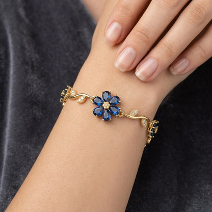 Gold bracelet with blue flower-shaped gemstones on a wrist against a dark background