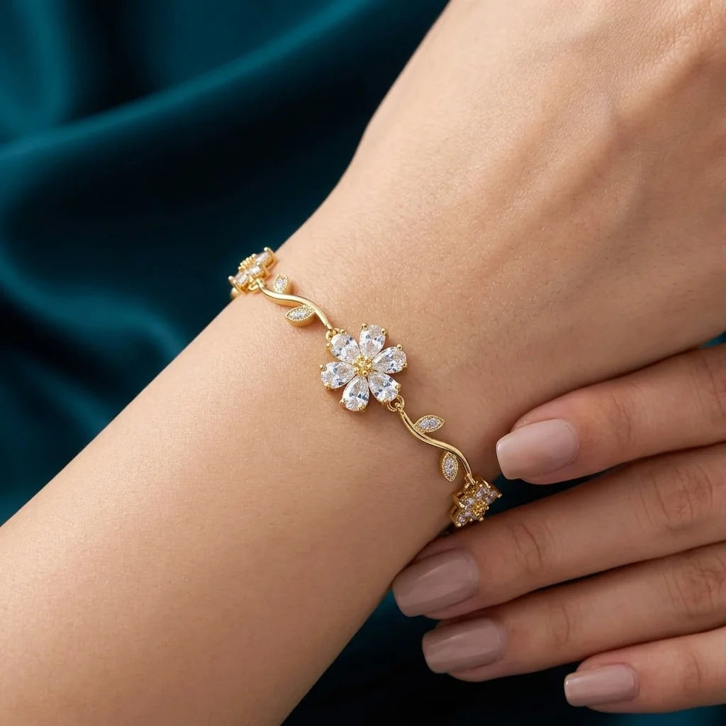Gold bracelet with floral design on a wrist against a dark blue fabric background