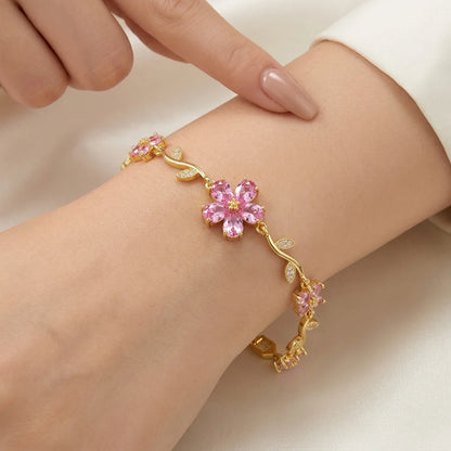 Gold bracelet with pink floral design on a wrist against a neutral background