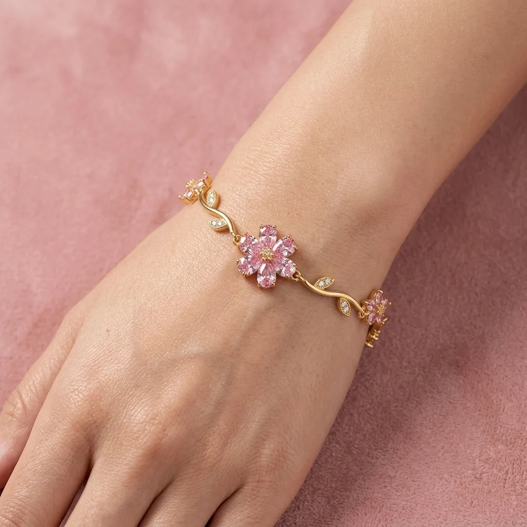 Gold bracelet with pink floral design on a wrist against a pink background