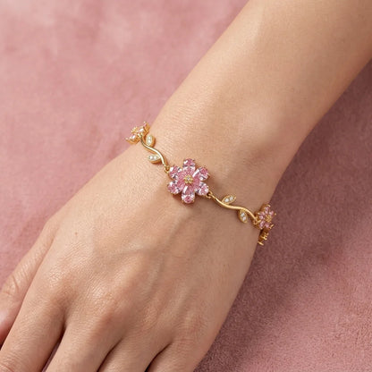 Gold bracelet with pink floral design on a wrist against a pink background