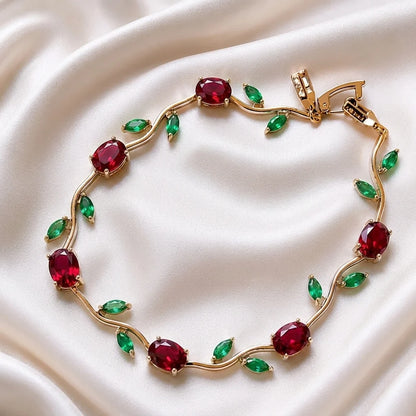 Gold bracelet with red and green gemstones on a white fabric background