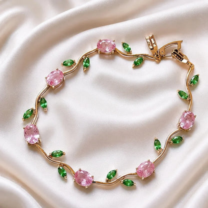 Gold bracelet with pink and green gemstones on a white fabric background