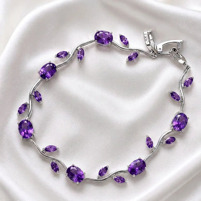 A silver vine-style bracelet adorned with oval and marquise-cut purple amethyst gemstones, displayed on a draped white satin fabric.