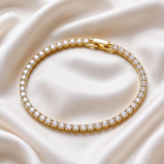A gold tennis bracelet with clear stones, arranged in a circle on a draped cream satin fabric background.