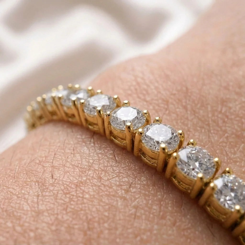A close-up of a yellow gold tennis ring with round brilliant-cut diamonds worn on a person's finger.