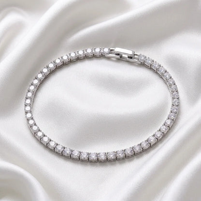 A silver tennis bracelet encrusted with clear cubic zirconia stones, arranged in a neat circle on a draped white satin fabric background.