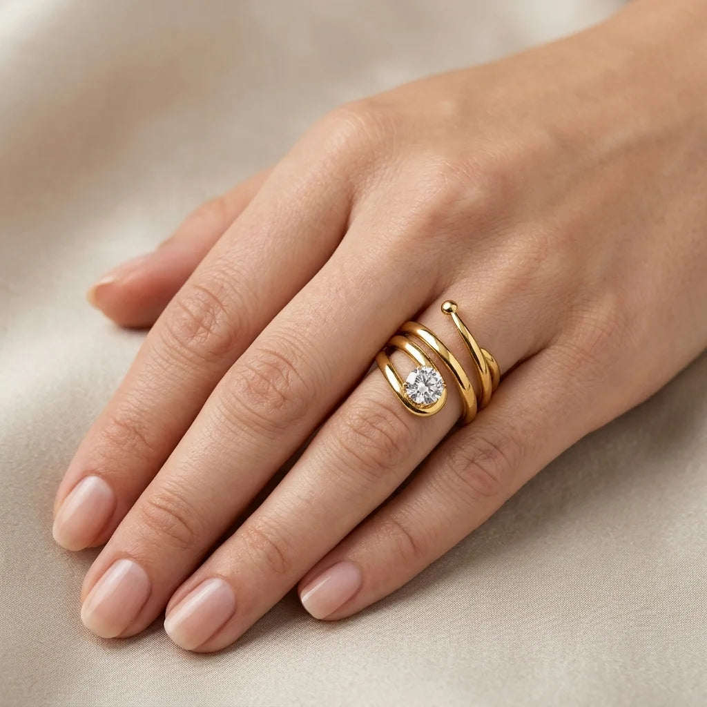 Elegant coil‑style gold ring featuring a prong‑set clear stone, worn on finger.