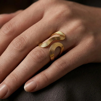 A close-up of a hand wearing a gold ring with a sculptural, flowing double-loop design.